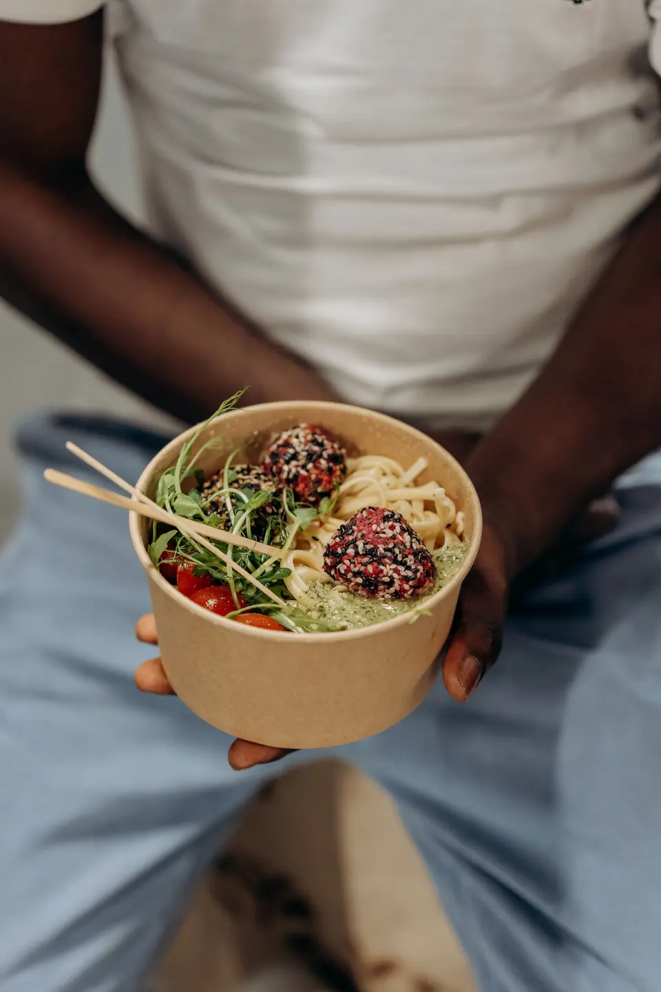 Noodles and meatballs in a kraft paper bowl held on a lap