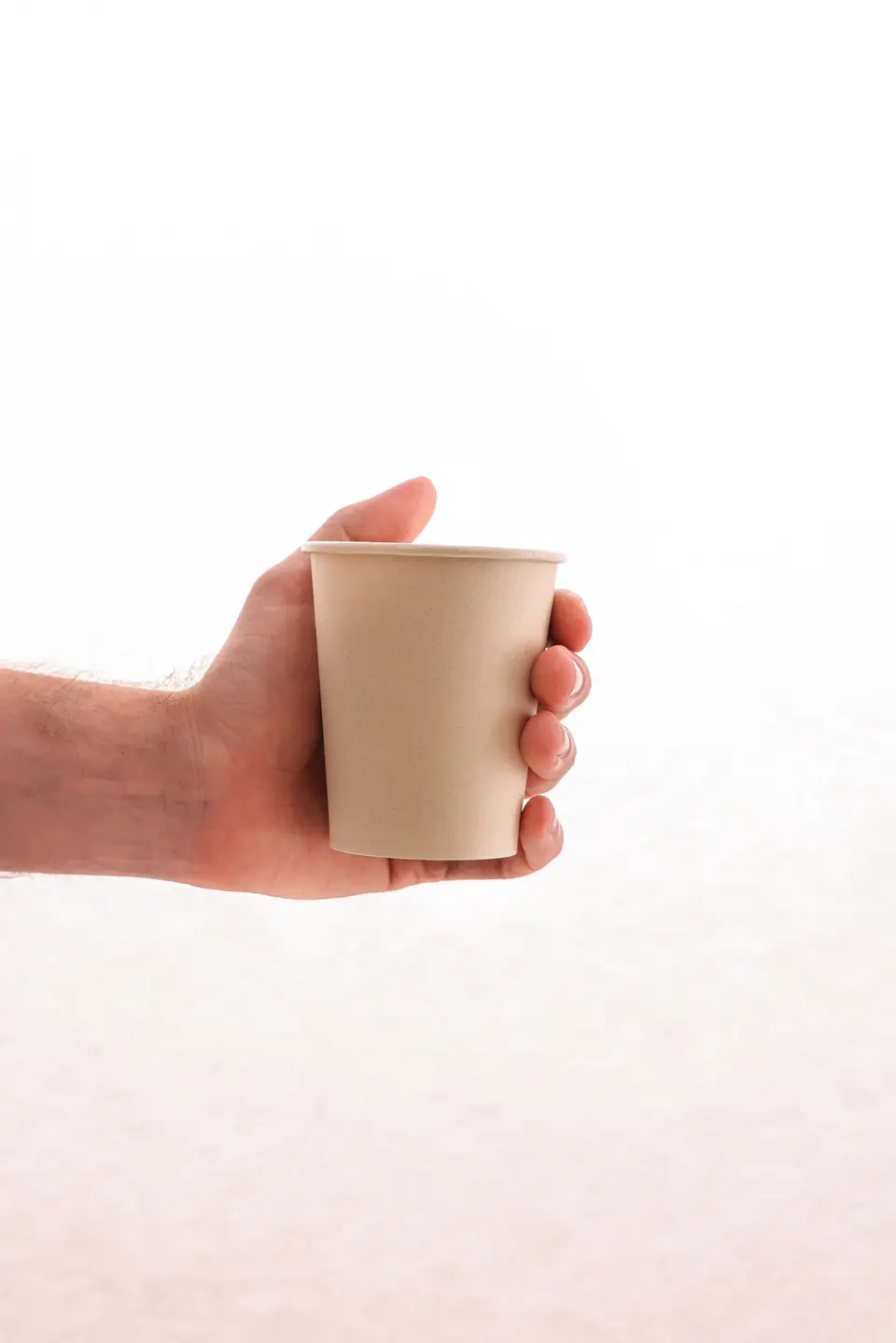 A hand holding a plain kraft paper cup