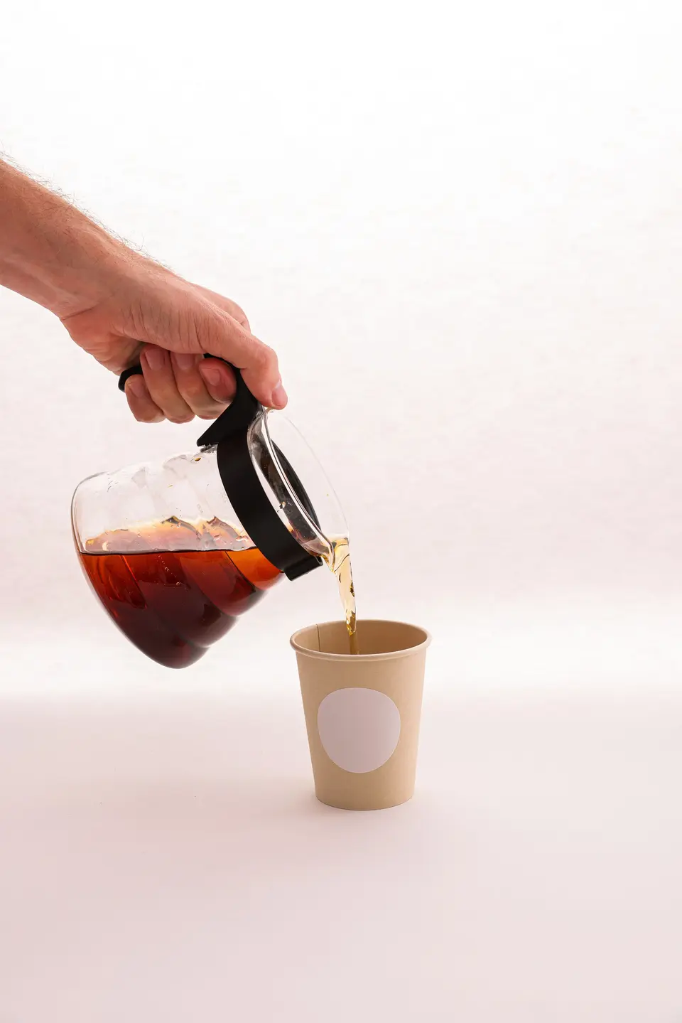 Coffee poured from a glass carafe into a kraft paper cup