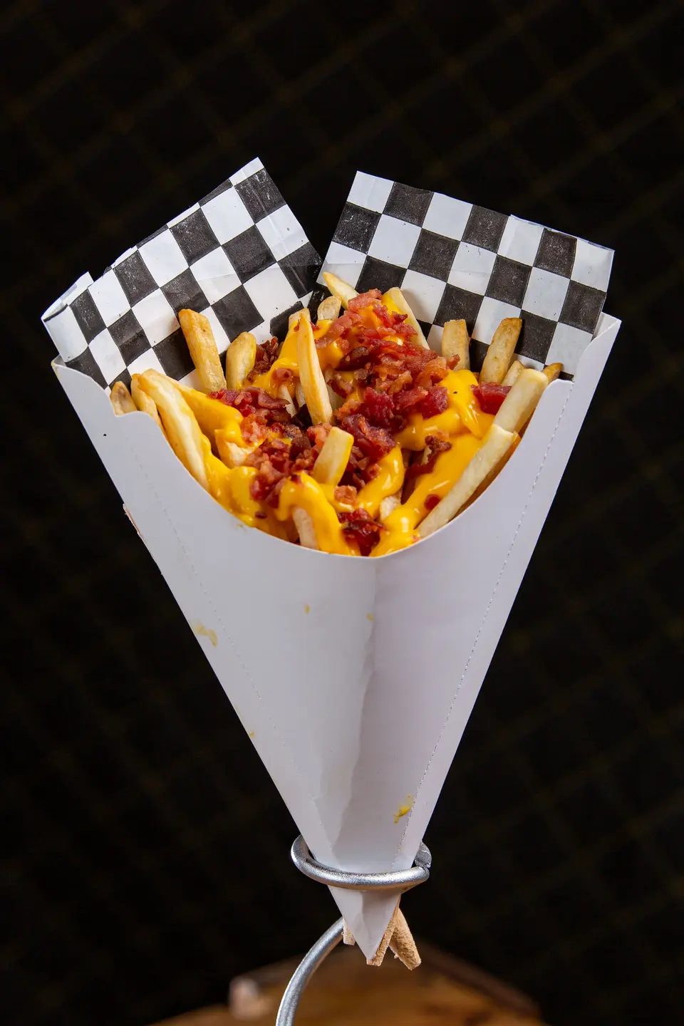 Loaded fries with cheese and bacon in a white paper cone