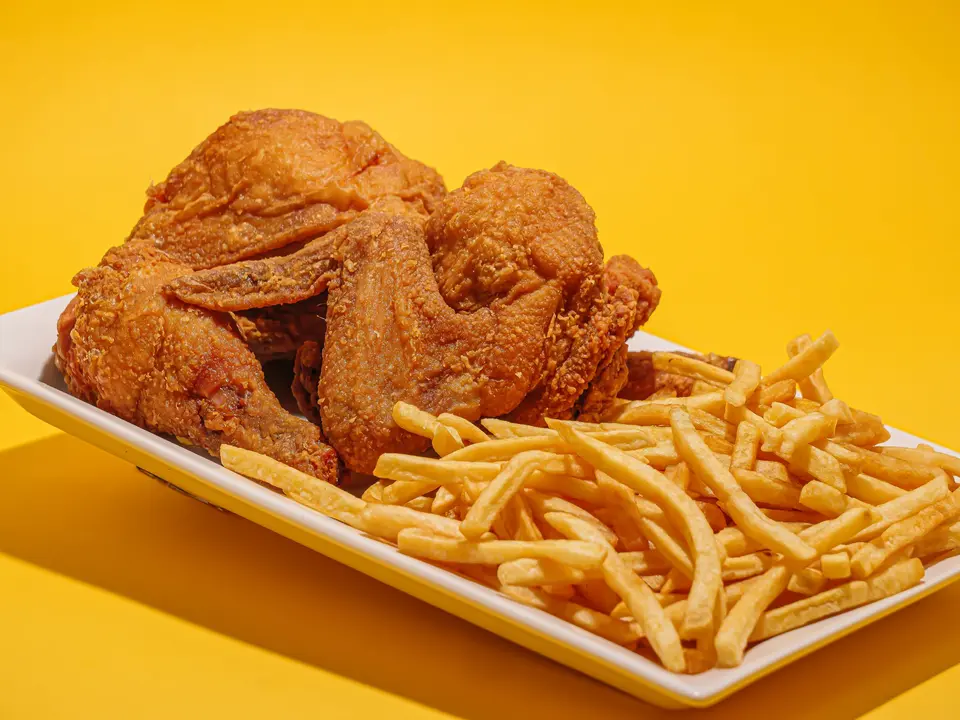 Fried chicken and a pile of fries on a white tray against a yellow wall