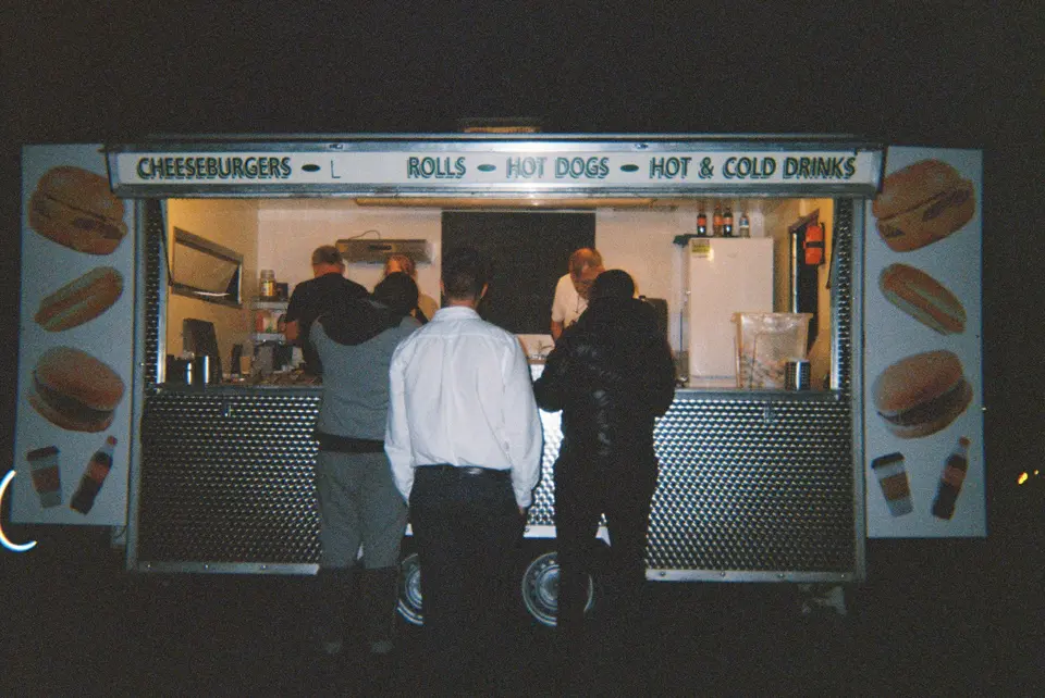 Customers ordering at a lit food trailer window at night