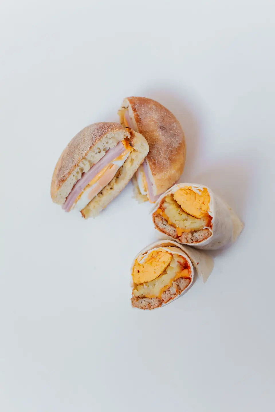 Wraps and a toasted sandwich cut in half on a white table
